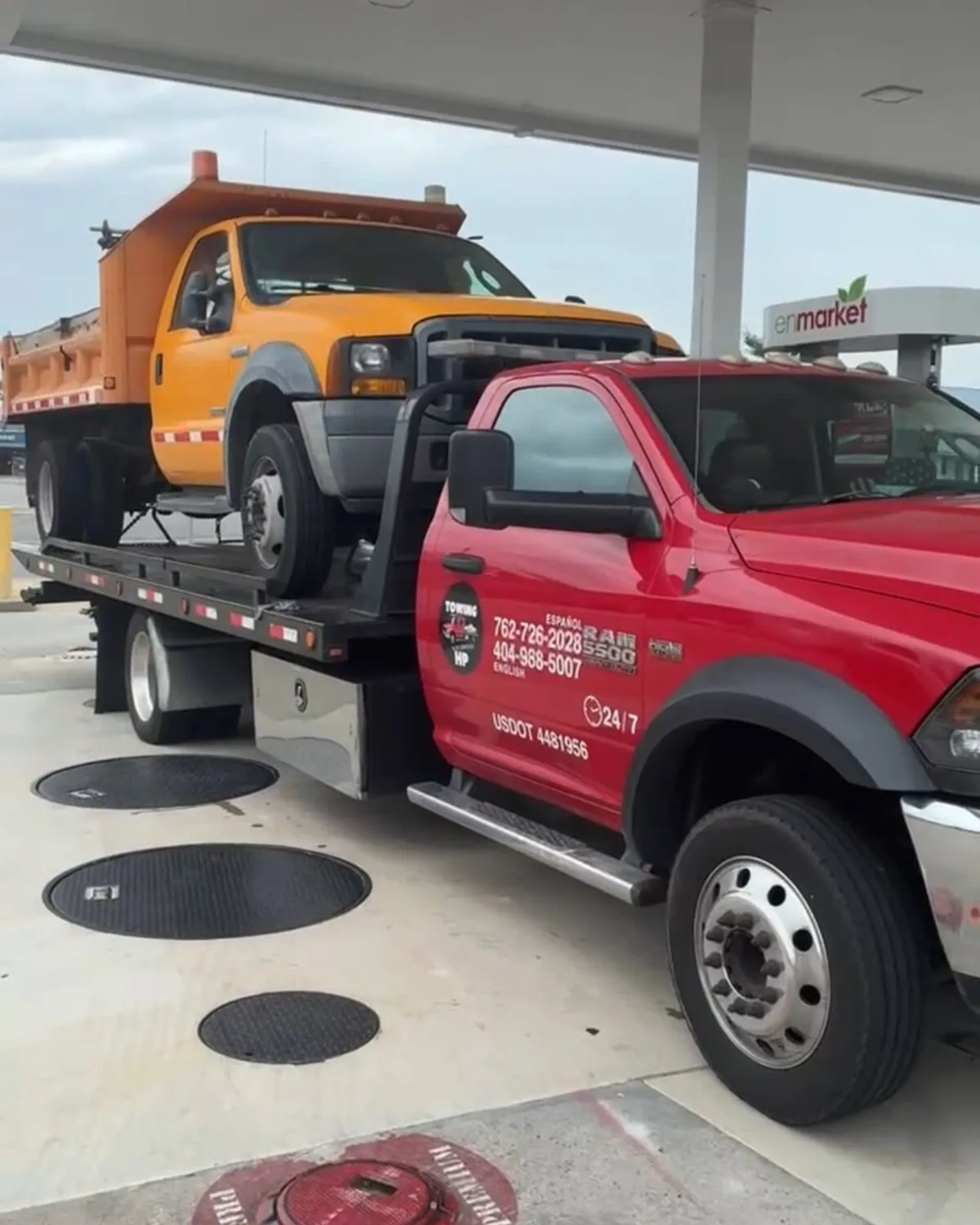 Red Ram flatbed tow truck transporting a yellow dump truck