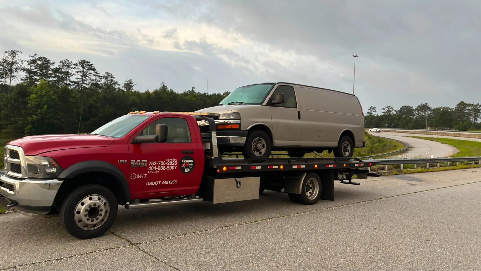 Red flatbed tow truck transporting a cargo van near an Atlanta highway