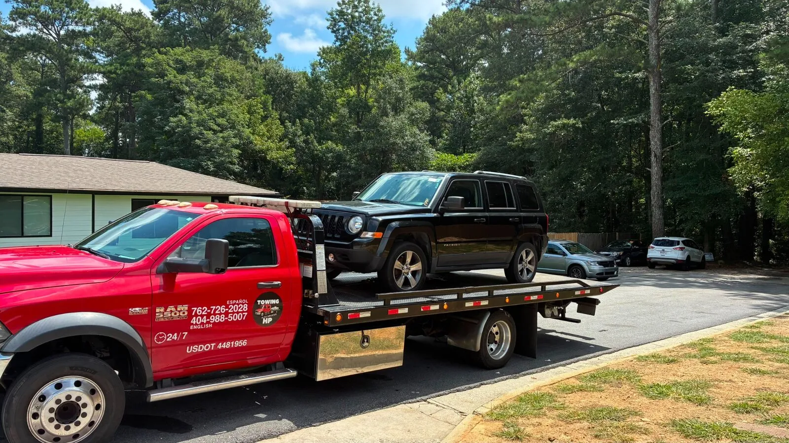 Red flatbed tow truck transporting a black Jeep SUV